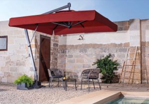 Parasol ogrodowy na tle budynku z pustaków i cegieł parasol antracytowy z boczna podstawa i czasza w kolorze bordo